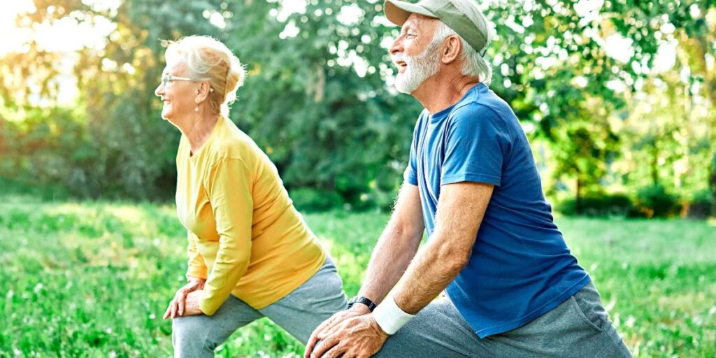 An active and happy senior couple stretches at the local park