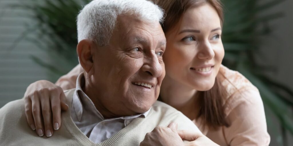 A senior man and his adult daughter smile and share a hug